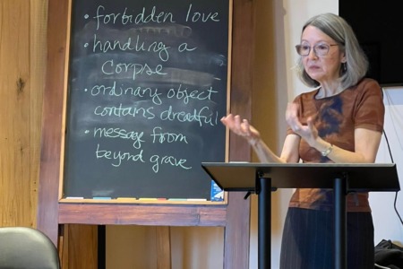 Photo of Naomi standing during class in Siena, Italy. Blackboard to her right lists Decameron-inspired writing prompts (e.g., "forbidden love," "handling a corpse").